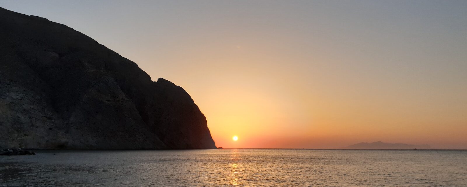 silhouette of mountain beside sea during sunset